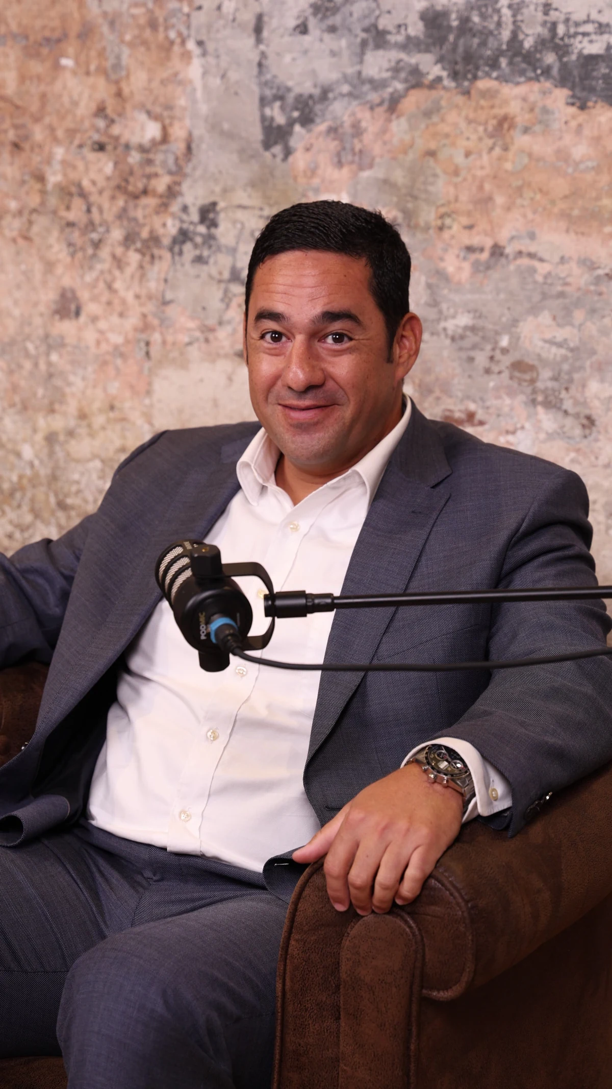 Alonso sonriendo en un sillón, con traje gris y camisa blanca.